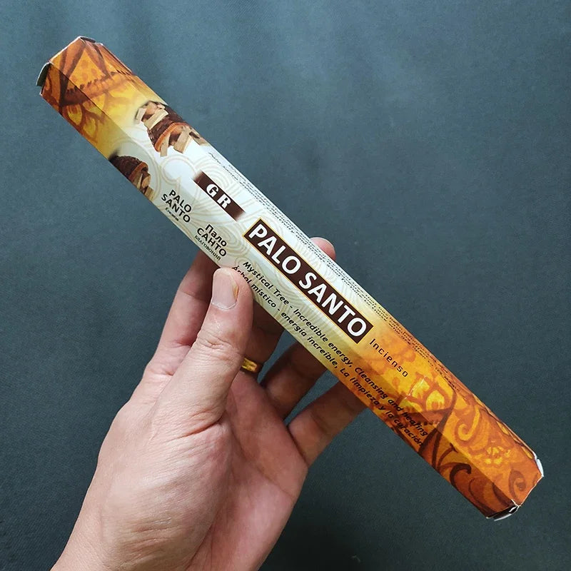 Hand holding a Palo Santo incense stick with packaging against a dark background