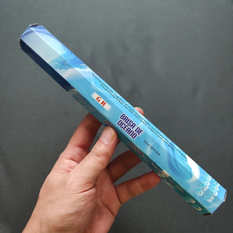Hand holding a blue incense stick box against a gray background