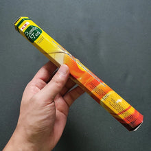 Hand holding a colorful cylindrical product with a brand label against a dark background