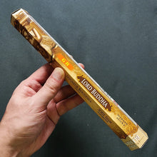 Hand holding a gold 'Lord Buddha' incense stick box against a dark background