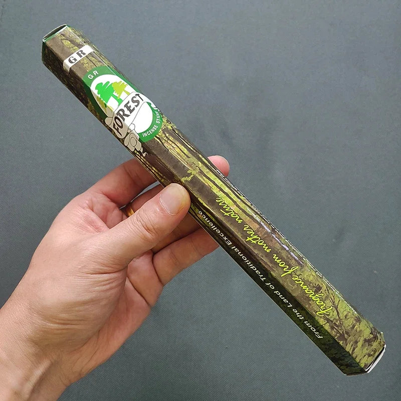 Hand holding a green incense box with a brand logo against a gray background