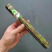Hand holding a green incense box with a brand logo against a gray background