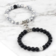 Two bracelets, one with white beads and silver accents, the other with black beads and silver accents, on a marble surface.