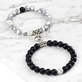Two bracelets, one with white beads and silver accents, the other with black beads and silver accents, on a marble surface.
