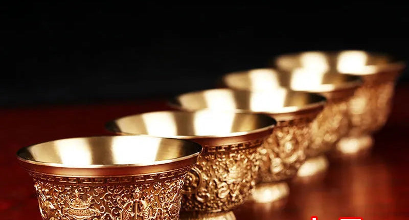 Set of gold cups with intricate designs on a red surface, against a black background with white text.