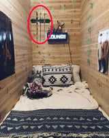 Small bedroom with wooden walls, a bed with patterned bedding, and a 'Lounge' sign on the wall.