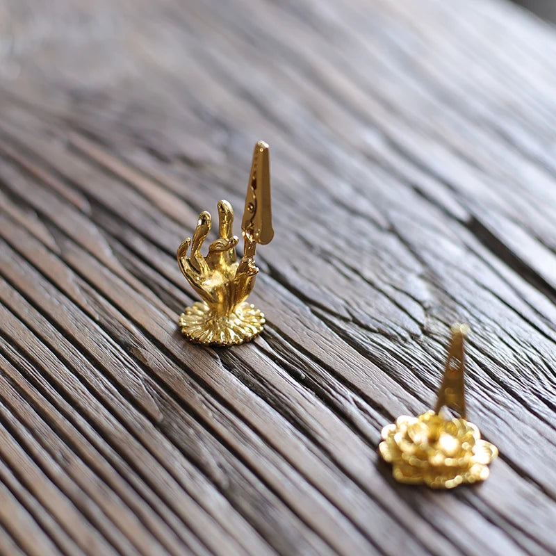 Gold hand and flower earrings on a textured surface