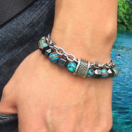 Bracelet with blue and black beads on a wrist by a body of water