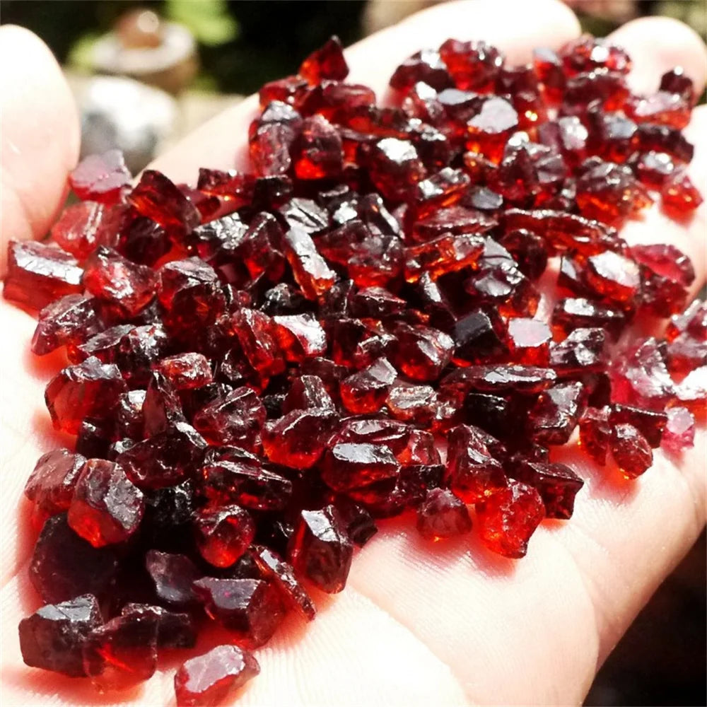 Hand holding a pile of red crystal-like stones against a blurred natural background