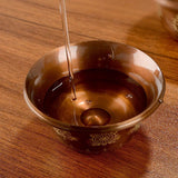 Brown liquid being poured into a decorative bowl on a wooden surface