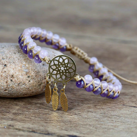 Bracelet with purple and white beads and gold dreamcatcher charm on a wooden surface