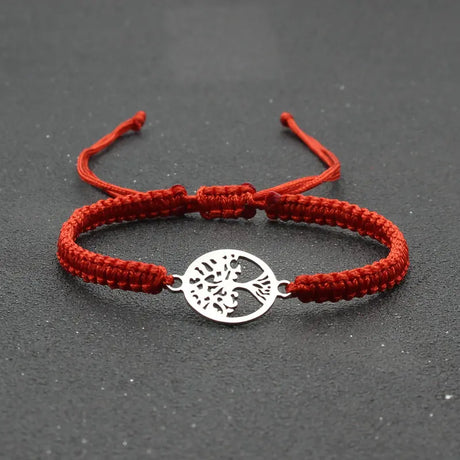 Red braided bracelet with a silver tree of life charm on a dark surface