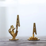 Gold hand-shaped clip and gold clothespin on a wooden surface with a light gray background