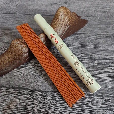 Orange incense sticks with a cylindrical container on a wooden surface