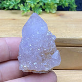 Crystal rock held in a hand with a wooden surface and greenery in the background