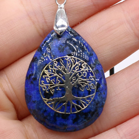 Blue teardrop-shaped pendant with tree of life design held in a hand