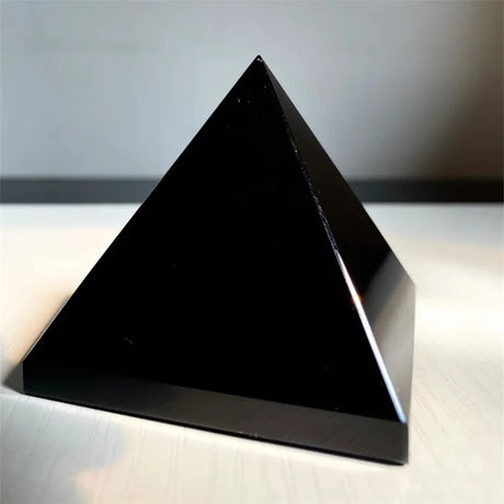 Black pyramid-shaped object on a reflective surface with a blurred background