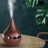 Wooden diffuser emitting steam on a wooden table with a dark wall and plant in the background