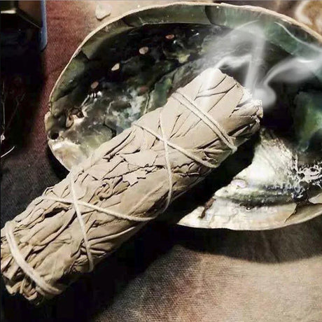 Rolled sage smudge stick on a stone surface with smoke rising