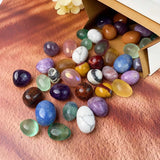 Assorted colorful gemstones spilling out of a cardboard box on a wooden surface.