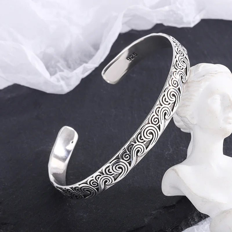 Silver bracelet with intricate patterns on a dark surface with a white fabric background