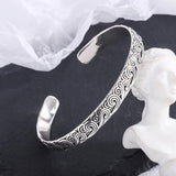 Silver bracelet with intricate patterns on a dark surface with a white fabric background
