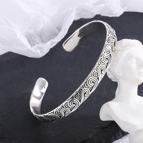 Silver bracelet with intricate patterns on a dark surface with a white fabric background