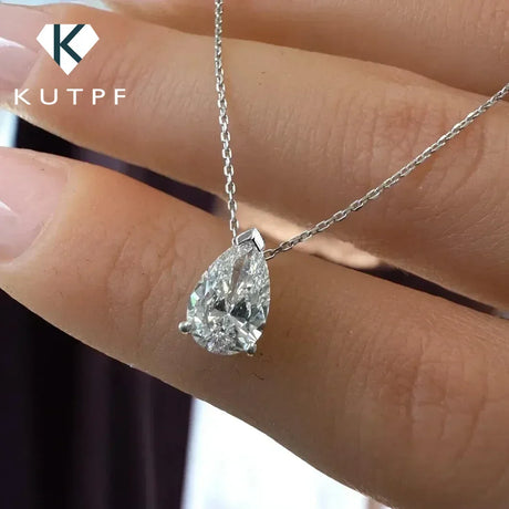 Teardrop-shaped diamond pendant on a chain held by a hand, with 'KUTPF' branding.