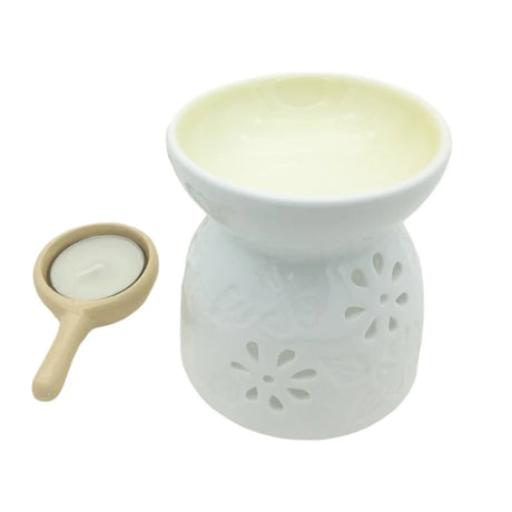 White ceramic oil burner with floral designs and a small beige holder with a candle on a white background