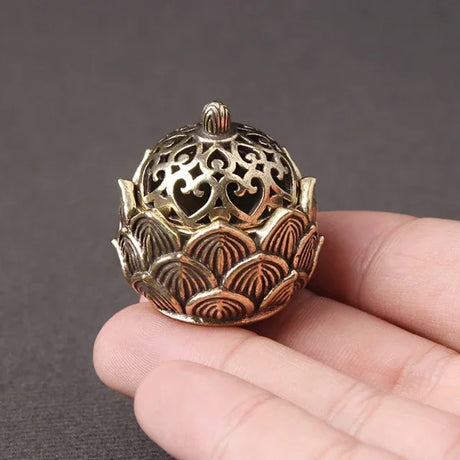 Decorative bronze incense holder held in a hand against a dark background