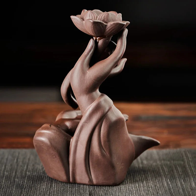 Ceramic sculpture of a hand holding a lotus flower on a wooden surface.