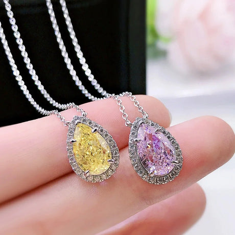 Two diamond pendants, one yellow and one pink, held between fingers against a blurred background.
