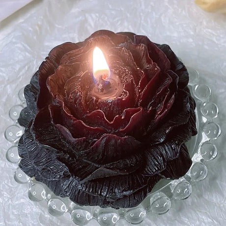 Rose-shaped candle with a lit center on a textured white surface