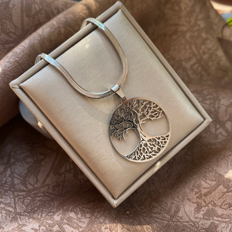 Silver tree of life pendant necklace in a box on a textured surface