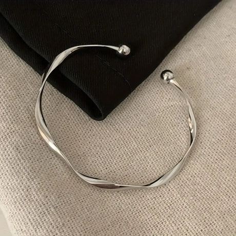 Silver bracelet on a textured beige surface with a black fabric background