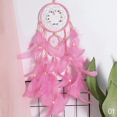 Pink dreamcatcher with feathers against a white wall