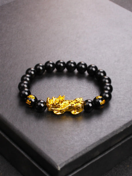 Black beaded bracelet with a gold dragon charm on a dark surface