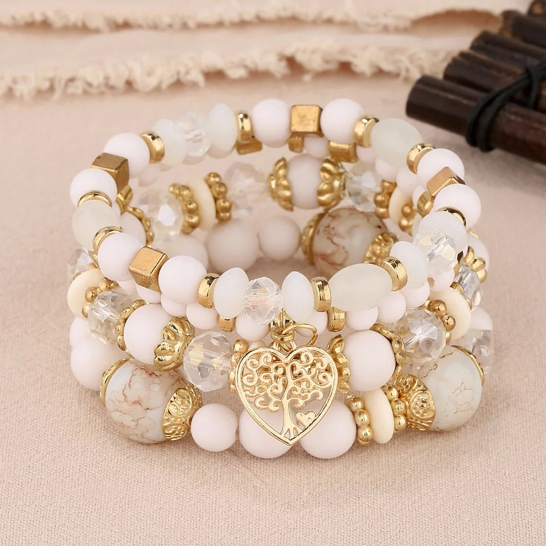 Stack of white and gold beaded bracelets with a heart charm on a beige fabric background