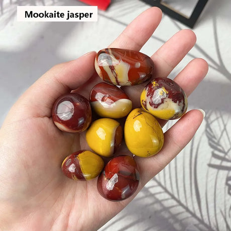Hand holding mookaite jasper stones with a neutral background