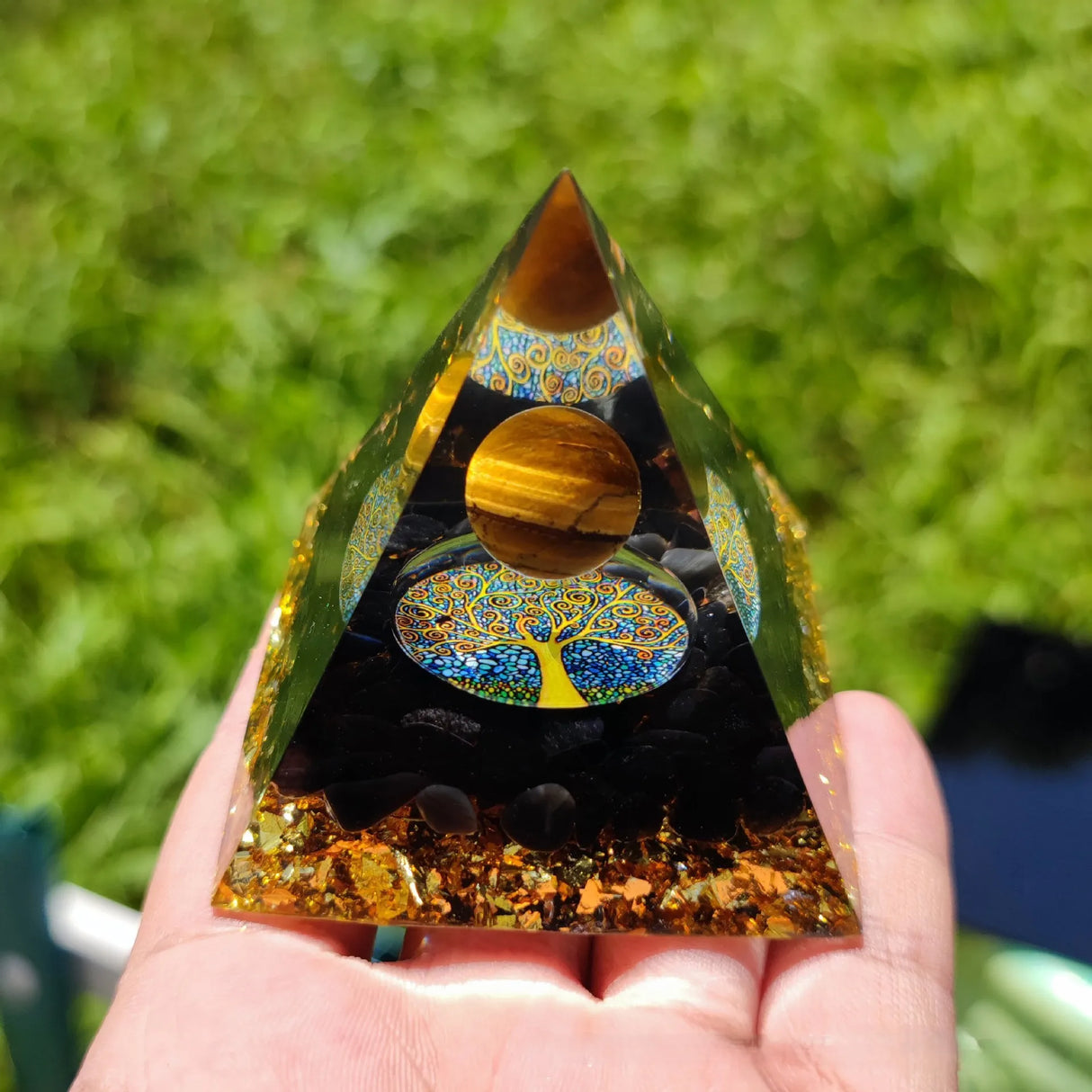 Decorative pyramid with tree of life design held by a hand against a blurred green background