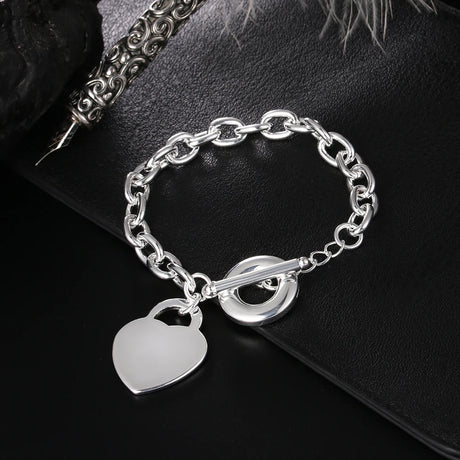 Silver chain bracelet with heart and lock charm on a dark surface