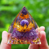 Pyramid-shaped crystal with a lotus flower design held by a hand against a green blurred background