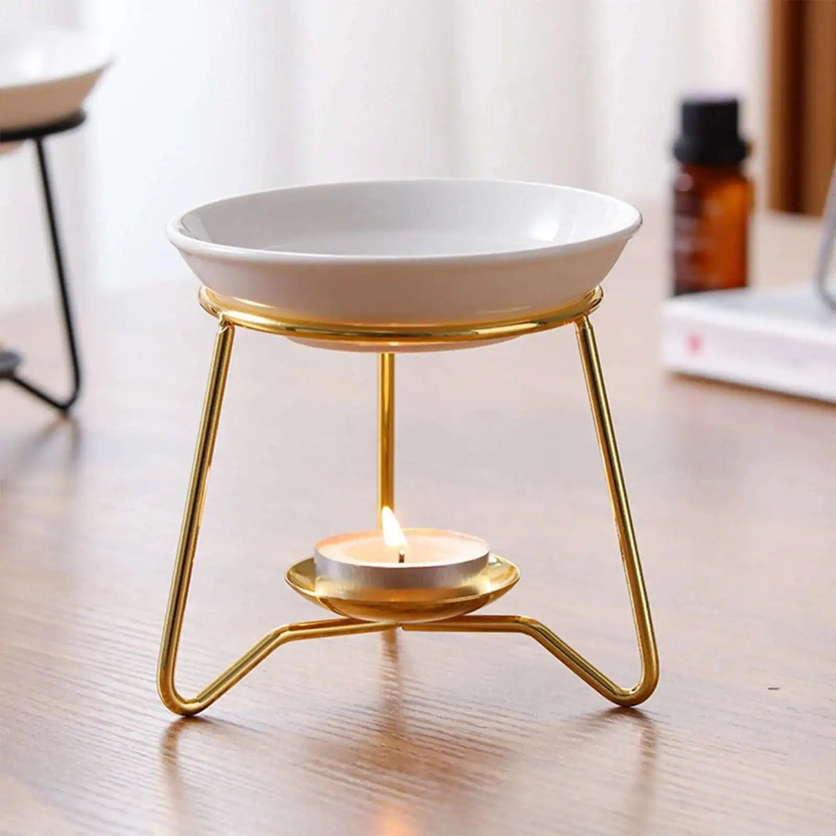 White ceramic bowl on a gold metal stand with a lit candle inside, on a wooden surface.