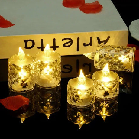 Set of small lit candles in clear holders on a reflective surface with a decorative background.