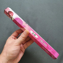 Hand holding a pink orchid incense stick box against a gray background