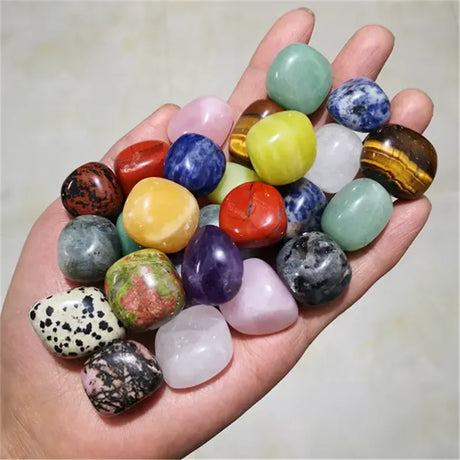 Hand holding a collection of multicolored gemstones against a neutral background