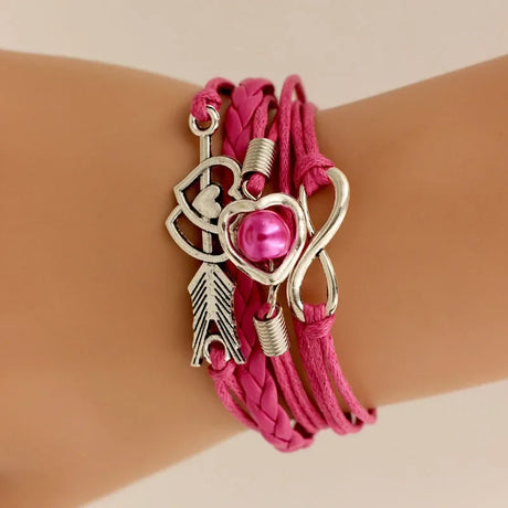 Pink bracelet with silver charms on a wrist against a beige background