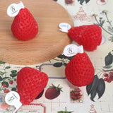Red strawberry-shaped candles on a wooden board with a floral patterned background