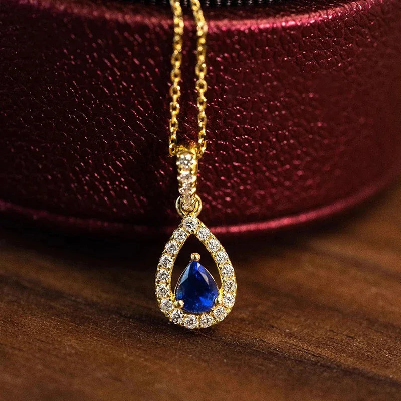 Gold necklace with a blue teardrop pendant on a wooden surface
