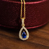 Gold necklace with a blue teardrop pendant on a wooden surface